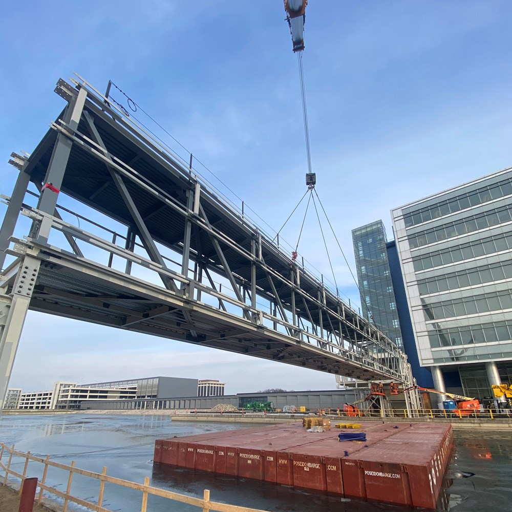 A crane lifts sections of the GM Technical Center Pedestrian Bridge.